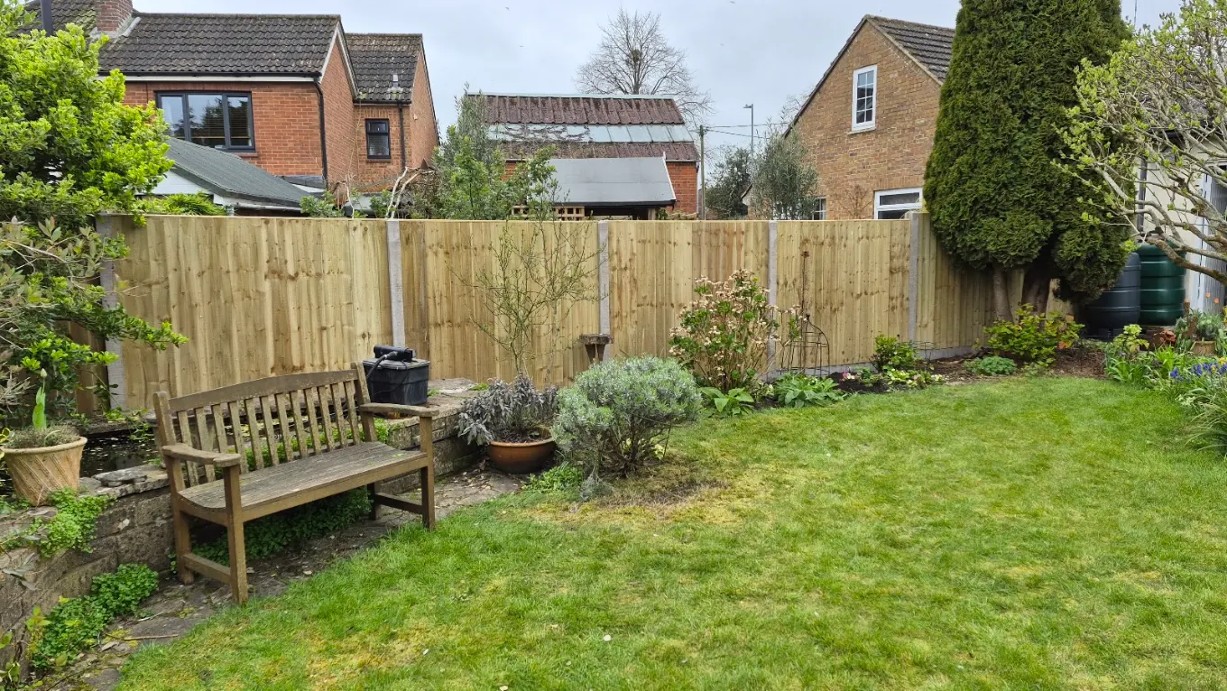 Close board fencing behind a pond and timber bench seat